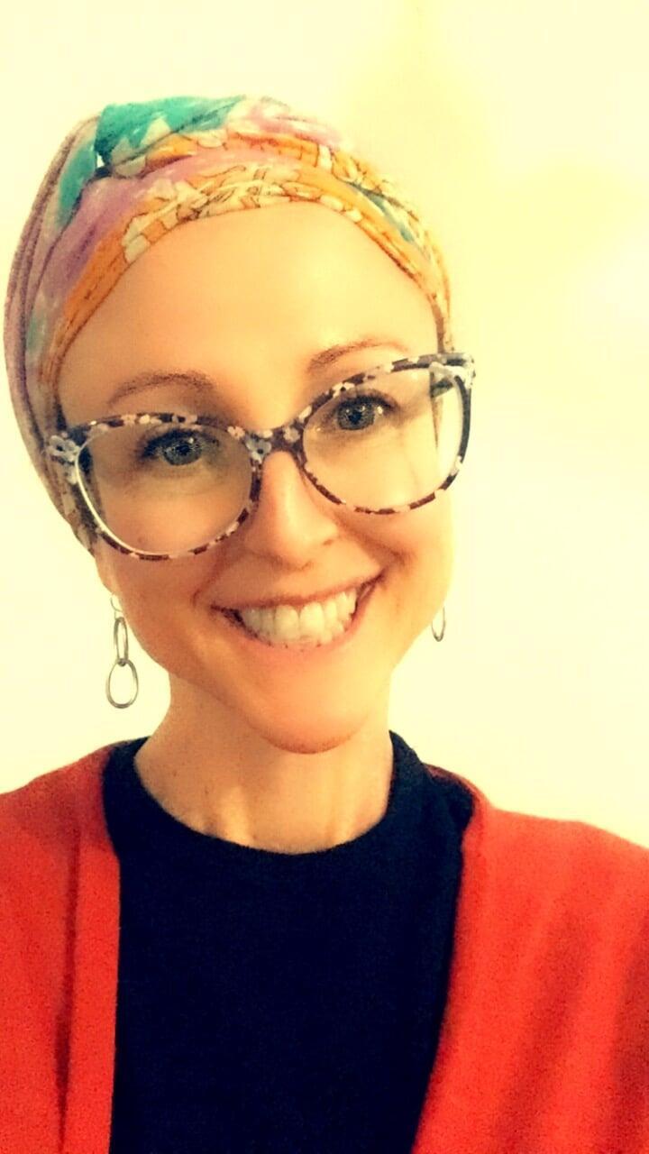 Photo of Brooke Lever wearing a black and orange top and a scarf in her hair with seeing glasses