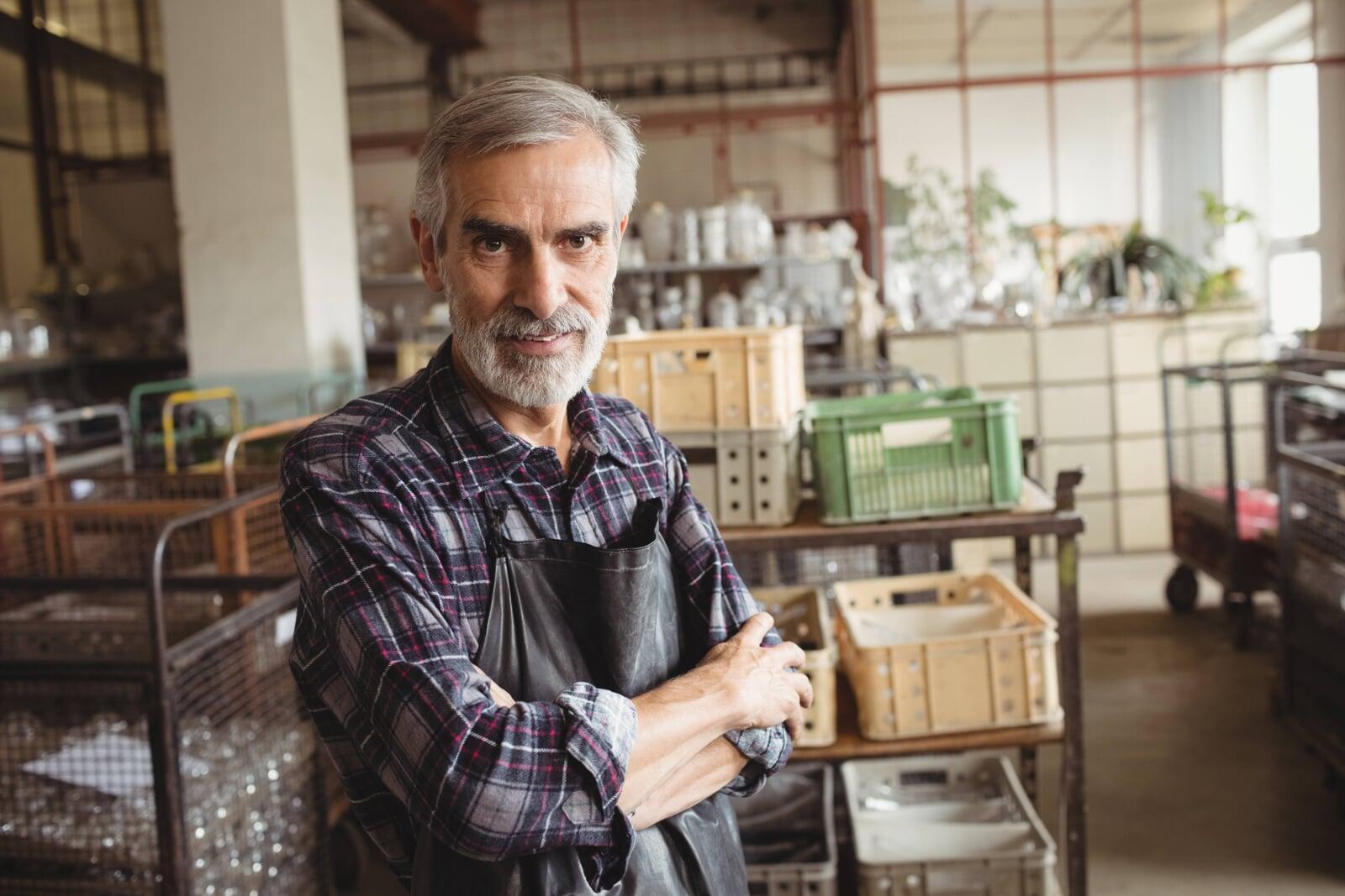 Photo of a person with an apron on standing in front of a warehouse with crates and packaging around them.
